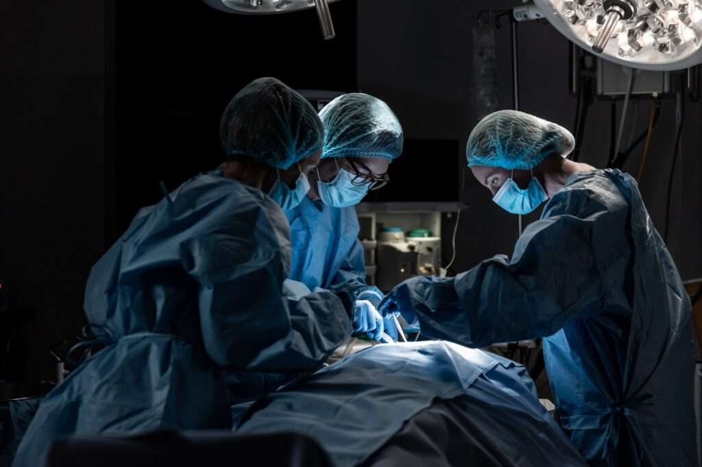 Diverse group of male and female surgeons in operating theatre wearing face masks performing surgery